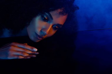 Suya dokunan muhteşem kadın koyu morötesi mavi ışıkta yansımasına bakıyor..