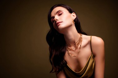 Kuyumcu reklamındaki kuyumcu bayan kahverengi gradyan arka planında altın kolye ile tanıtım yapıyor..