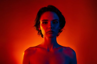 Güzel bir kadının çıplak omuzlarının fotoğrafı. Cilt bakımı prosedüründen zevk alıyor. Kırmızı neon rengi arka plan..