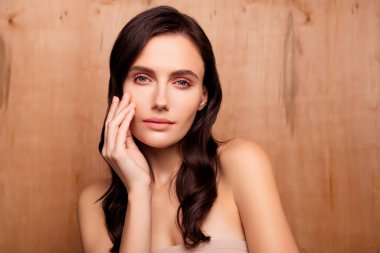 Esmer bukleli bir kadının fotoğrafı. Yüzüne dokunuyor. Deri yanakları ahşap arka planda izole edilmiş..