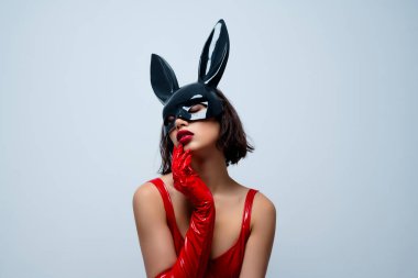 Çekici bir kadının fotoğrafı dokunaklı yüz derisi tavşan maskesi açık gri arka planda izole edilmiş kırmızı deri kıyafetler..