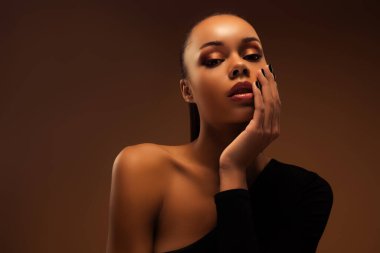 Çekici, şehvetli, nazik kadının fotoğrafı. Yüze dokunmak, dekoratif makyaj, bej rengi arka planda izole edilmiş..