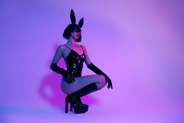 Siyah deri elbiseli tavşan kostümlü bir kızın fotoğrafı izole edilmiş neon filtre arka planı pozu veriyor..