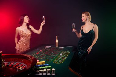 İki güzel kadın satıcının ve oyuncunun fotoğrafı neon arka planda 21 oynadıktan sonra şampanya içiyorlar..