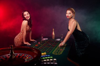 İki lüks bayanın fotoğrafı neon arka planı izlemeden rulet oynayıp blöf yapıyor..