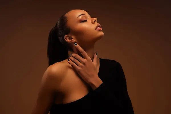 Sevimli, güzel, tatlı, sataşan bir bayanın fotoğrafı. Boynuna dokun. Bej renkli arka planda izole edilmiş bir arzu hisset..