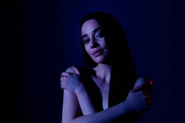 Çekici bir kızın kendine sarılma fotoğrafı. Vücuda dokunma. Koyu neon rengi arka plan..