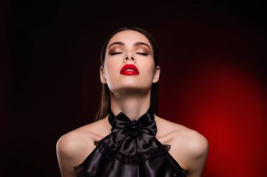 Parlak makyajlı bir kadının fotoğrafı. Gözleri kapalı. Arzularını izole edilmiş kırmızı bir arkaplan..