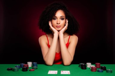 Pokerde güçlü genç bir kadının fotoğrafı. Masada koyu pembe arka planda bir sürü çiple oturuyor..