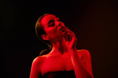 Çekici, çıplak omuzlu, dokunaklı, izole edilmiş siyah turuncu ışıklı arka plan..