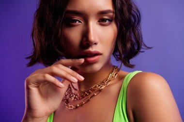 Asyalı bir kadının pofuduk dudaklarına dokunurken çekilmiş bir fotoğrafı canlı mor arkaplan gibi görünüyor..