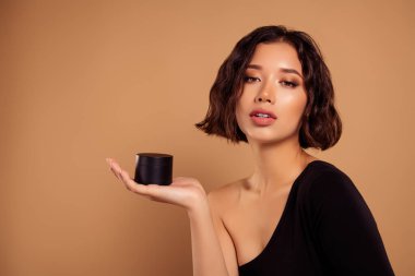 Baştan çıkarıcı bir kadının omuz üstü giyinmiş fotoğrafı. Saç maskesini destekleyen, tenha kahverengi bir arka plan..