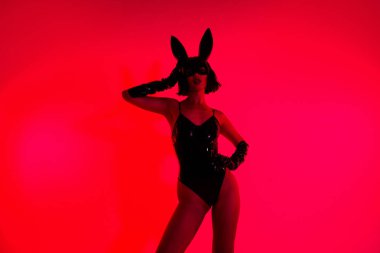 Siyah deri ceket giyen bir kızın fotoğrafı. Dokunmatik tavşan maskesi takıyor. İzole edilmiş kırmızı arka plan..