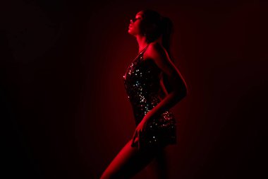 Profil tarafı, pullu Afrikalı bir kızın fotoğrafı. Elbise giysisi, bacağa dokun. Tutkulu, izole kırmızı kolo arka plan..