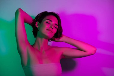Çekici, güzel bir kızın fotoğrafı. Başı kapalı, gözleri kapalı. Neon renkli arka planda eğlenmeye bakın..
