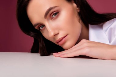 Beyaz masaya yaslanmış bir kadının fotoğrafı. Yumuşak, çekici, soyutlanmış pembe bir arka plan..