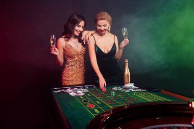 Kumarhanede poker oynayan iki göz kamaştırıcı kadının fotoğrafı neon ışıklı arka planda siyah bir numara üzerine bahse girmişler..