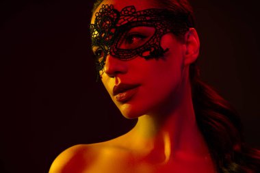 Tutkulu modelin çıplak omuzlarının kesilmiş fotoğrafı dantel maske boş alana takılıyor izole edilmiş siyah neon ışık arka planı.