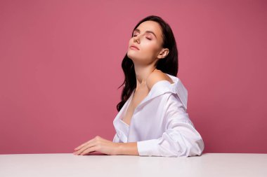 Kızın fotoğrafı. Masaya yakın, gözleri kapalı. Şefkat, izole edilmiş pastel arka plan..