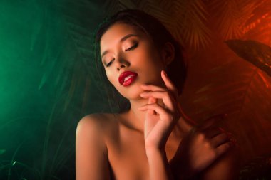 Göz kamaştırıcı kız portresi el parmakları pürüzsüz yüze dokunur neon ışıklı duman orman bitkileri arka planda.