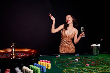 Pahalı elbiseli güzel bir kadının fotoğrafı Blackjack turnuvası sırasında koyu arkaplanda şampanya içiyor..