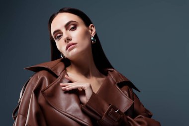 Göz kamaştırıcı, kahverengi deri ceketli, koyu gri arka planda, çekici bir kadının portre çekimi..