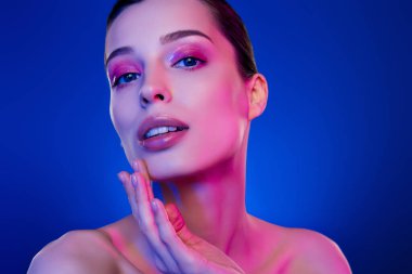 Muhteşem, şık bir kadının fotoğrafı. Yüzüne parmağıyla dokun. Ayrı, neon rengi arka plan..
