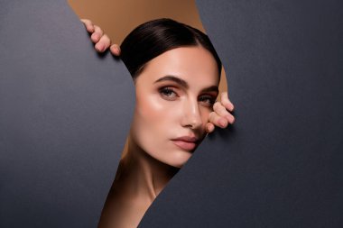 Gri arka planda izole edilmiş kağıdın üzerinde saklanan alımlı, alımlı, göz kamaştırıcı kadının fotoğrafı..