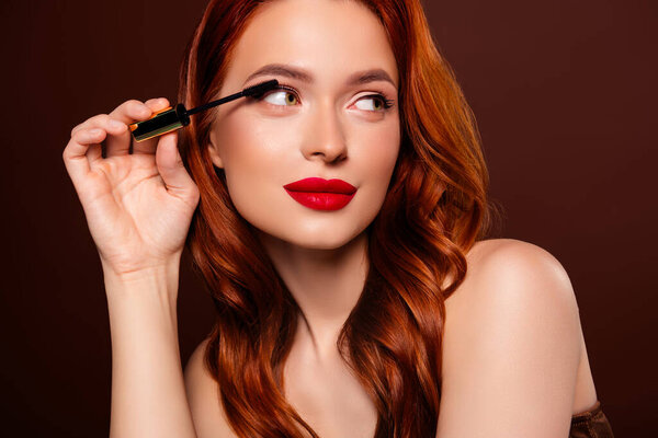 Close up photo of alluring attractive lady applying mascara preparing party isolated on brown color background.