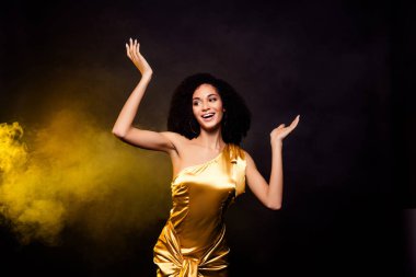 Çekici, güler yüzlü, altın elbiseli bir bayanın dans ederken çekilmiş fotoğrafı..