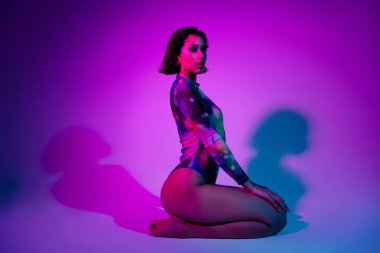 Baştan çıkarıcı seksi kadının fotoğrafı. Renkli bir beden giy. Dizlerinin üstüne çök..