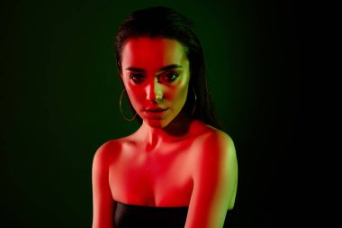 Göz kamaştırıcı, kendine güvenen, boş alan pozu veren, neon ışıklı arka planda izole edilmiş bir kızın fotoğrafı..