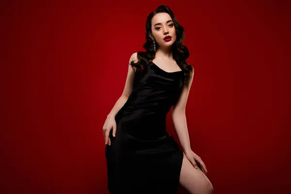 Çekici, çekici bir kadın modelin kırmızı arka planda izole edilmiş siyah elbiseli hali..