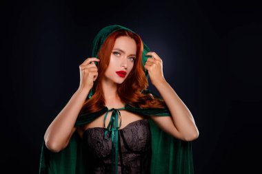 Koyu renkli sihirbaz kadının fotoğrafı cezbedici hissediyor. Yeşil başlık ve izole edilmiş siyah kapüşon giyiyor..