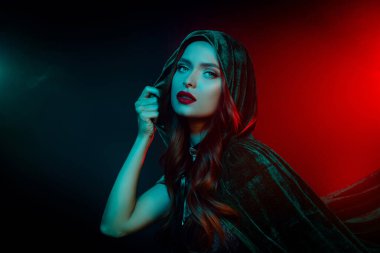 Göz kamaştırıcı bir kadının fotoğrafı yeşil pelerinli, cadılar bayramı için giyinmiş karanlık neon arka plan..