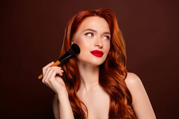 Gorgeous attractive lady applying foundation powder makeover empty space isolated on brown color background.