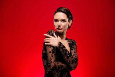 Kırmızı arka planda izole edilmiş siyah dantel elbiseli güzel bir kadın fotoğrafı..