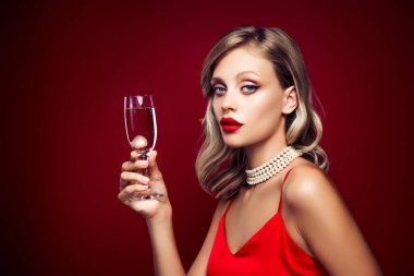 Çekici bir bayanın lüks içinde dinlenirken çekilmiş fotoğrafı kırmızı arka planda izole edilmiş şarap kadehi tutan modaya uygun elbiseler giyer..