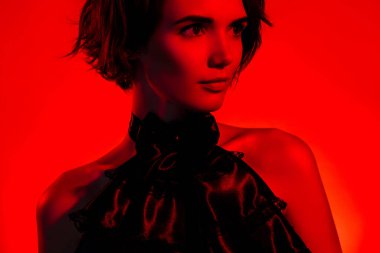 Kırmızı neon arka planda izole edilmiş cadılar bayramı partisini kutlayan büyüleyici bayan stili siyah yakalı fotoğraf..