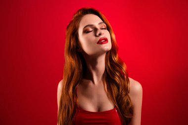 Güzel, çekici, kapalı gözlerinin fotoğrafı kırmızı arka planda izole edilmiş seksi deri elbiseler giymekten zevk alıyor..