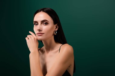 Çekici elbiseli, seksi bir bayanın yanak boşluğuna dokunduğu yeşil renkli bir arka plan..