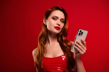 Çekici bir bayanın fotoğrafı. Telefon duruşu, eshop. Kırmızı arka planda izole edilmiş seksi deri kıyafetler..