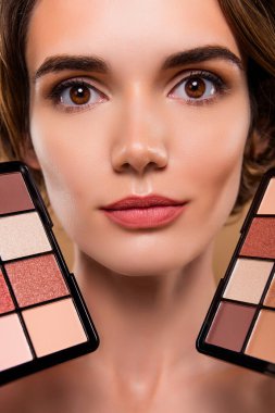 Çekici bir bayanın dikey kesilmiş fotoğrafı çıplak makyaj paletleri gösteriyor izole edilmiş bej arkaplan rengi.