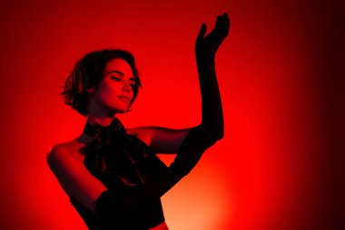 Kırmızı neon arka planda tiyatroda oynayan çarpıcı kadın oyuncunun fotoğrafı..