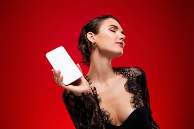 Seksi genç kız holding cihazının fotoğrafı beyaz ekran siyah elbise içinde cadılar bayramı partisinin kırmızı arka planı.