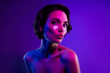 Çekici bir kızın fotoğrafı dudaklarını buruşturur. Gözlerinde kolajen pedler, parlak, neon bir arka plan var..