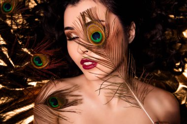 Şehvetli, çekici bir kızın yüksek açılı fotoğrafı altın folyo rengi arka planda izole edilmiş yumuşak tene dokunuyor..