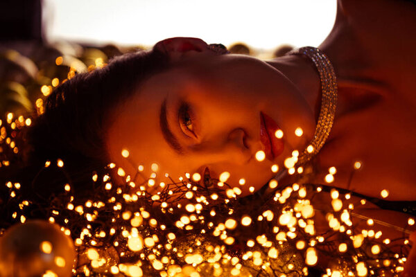 Pphoto of stunning lady lying on shiny backdrop covered decorated with xmas garlands lights.