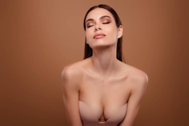 Esmer, saçları olan, gözleri kapalı bir kızın fotoğrafı. Şefkat duygusunu hisset. Sütyen ve izole edilmiş pastel arka plan kullan..