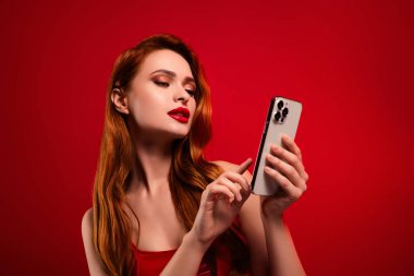 Çekici bayan holding cihazlarının online alışverişinin fotoğrafı kırmızı arka planda izole edilmiş seksi deri elbiseler..